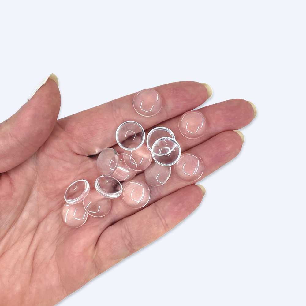 Handfull med 14 mm glascabochoner illustrerar storleken, klart glas