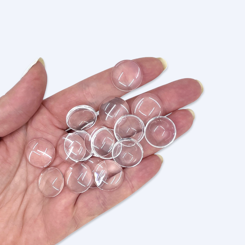 Handfull med 18 mm glascabochoner illustrerar storleken, klart kupigt glas