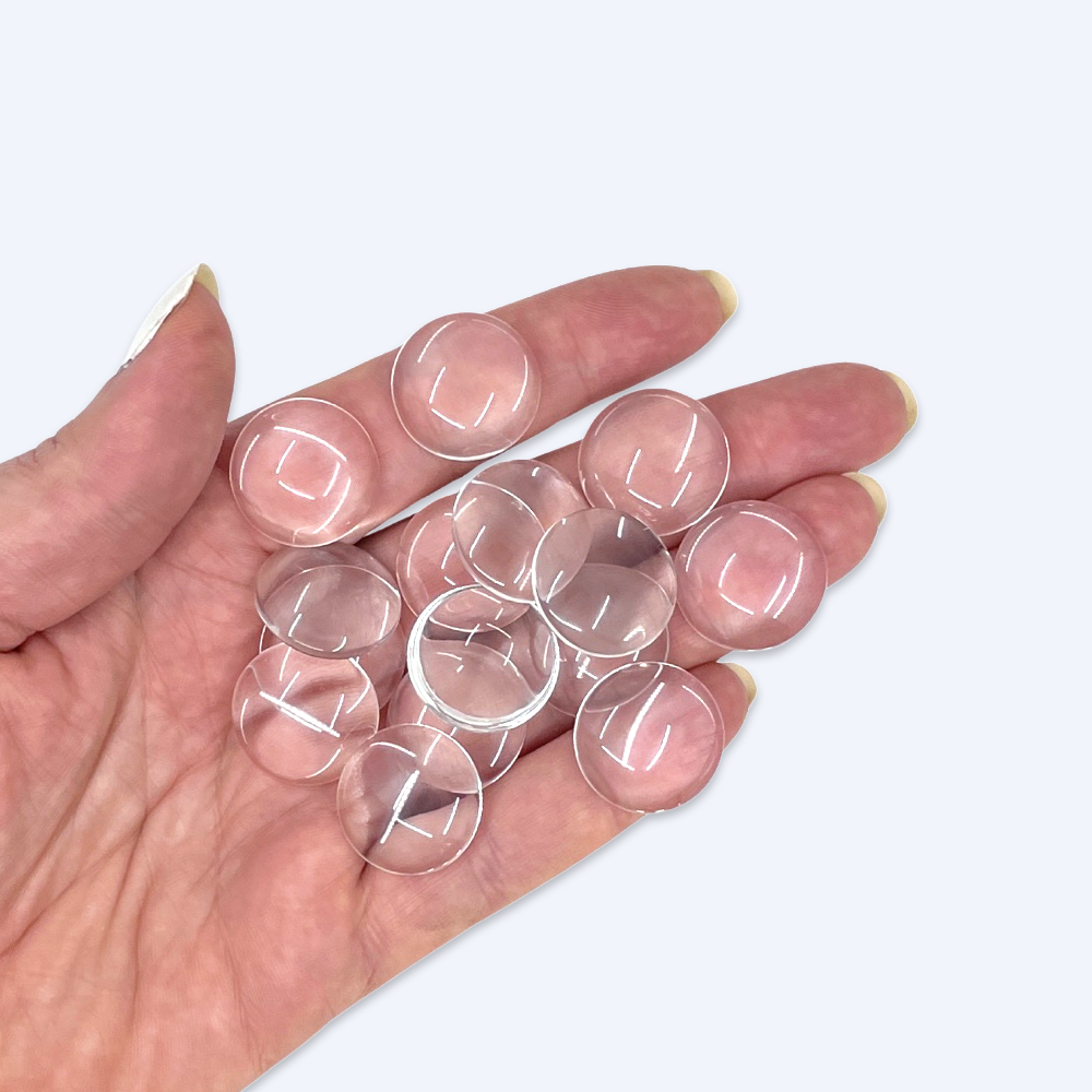 Handfull med 20 mm glascabochoner illustrerar storleken, klart kupigt glas
