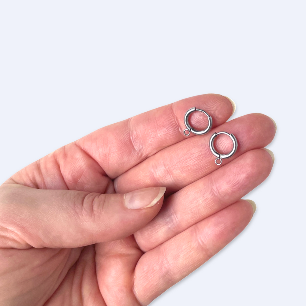 I handflatan ett par 12 mm huggie-ringar med upphängningsöglor, storlek illustrerad, kirurgiskt stål